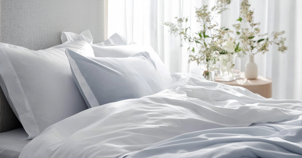 Crisp cotton sheets neatly made on a sunlit bed with white pillows and a vase of fresh flowers on the bedside table.