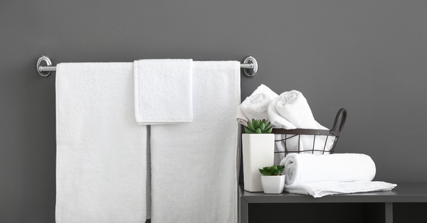 Stacked white bath towel set with matching hand and face towels, soap dish, and orchid on a marble surface.