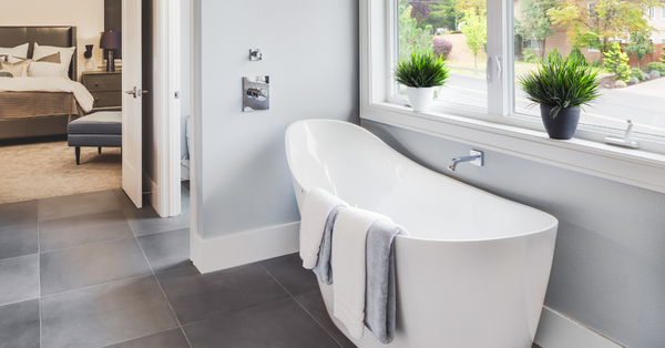 Spa-inspired bathroom with freestanding tub, sunlit window, and neatly folded white luxury bath towels on a wooden stool.