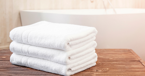 Neatly folded stack of large white bath towels resting on a wooden table, ready for a spa-like bath experience.