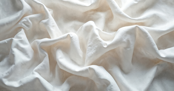Close-up of ivory luxury percale sheets draped in soft, airy folds.